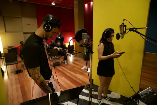 Dos artistas en la cabina de grabación de PKO Studios, con auriculares y micrófono